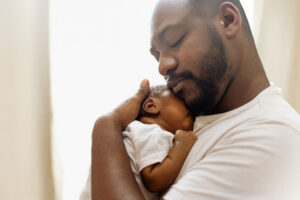 frican American father gently holds a newborn baby close, showing love, bonding, and family support.