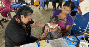 Healthcare professional uses a measuring tape to assess an infant while the child’s mother holds the baby during a community medical mission clinic.