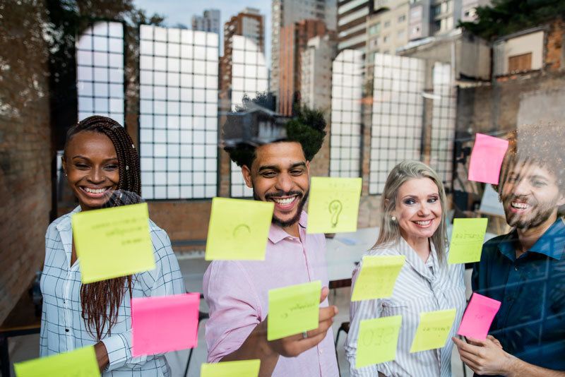Team works together with sticky notes on a glass wall, illustrating how to be creative through collaboration, concept development, and the creative process.
