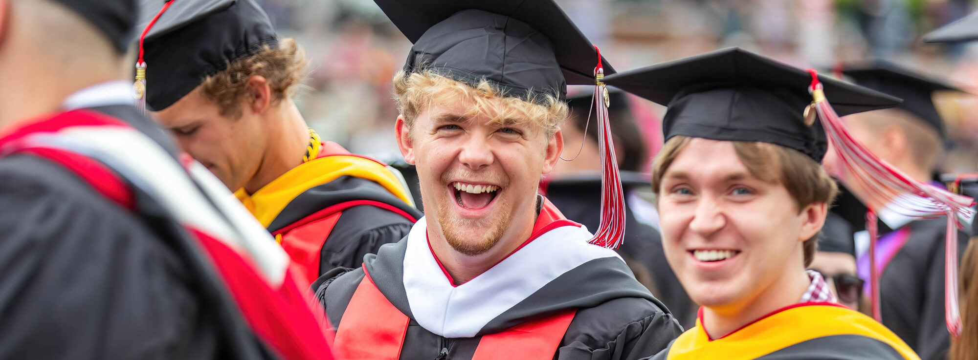 Two smiling graduates in caps and gowns celebrate in the commencement crowd, illustrating the student impact of Parent PLUS Loan changes.
