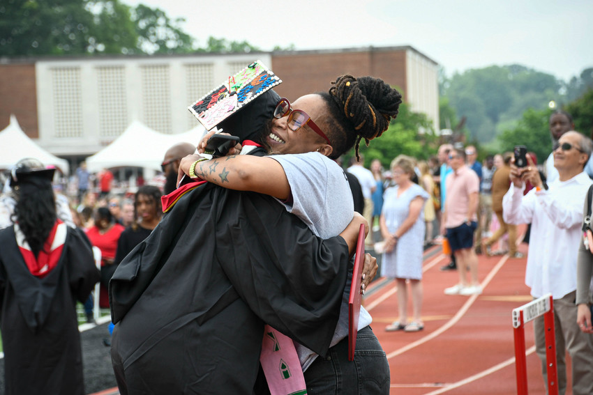 Graduate hugs a supporter after commencement on the track, reflecting how Parent PLUS Loan changes can affect families paying for college.