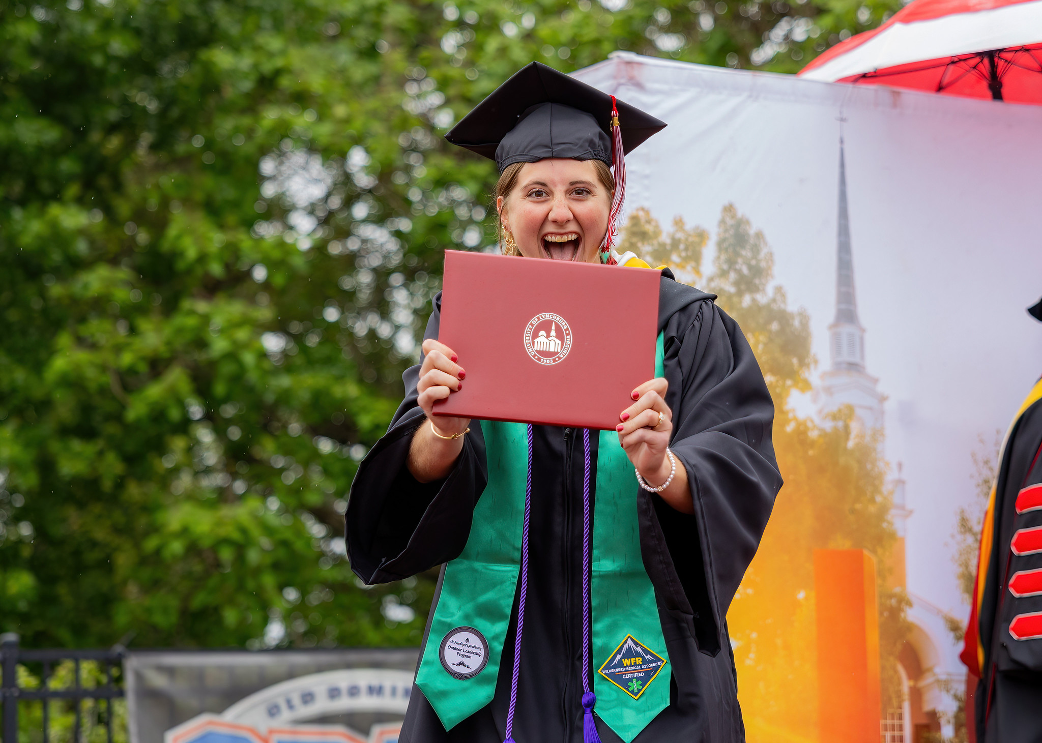A young woman wearing academic regalia holding a diploma and smiling.